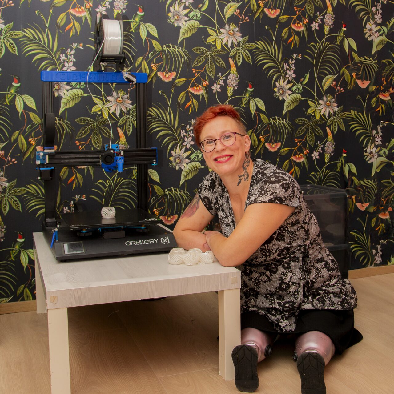 Proteeseja käyttävä nainen istuu 3D-tulostimen vieressä.