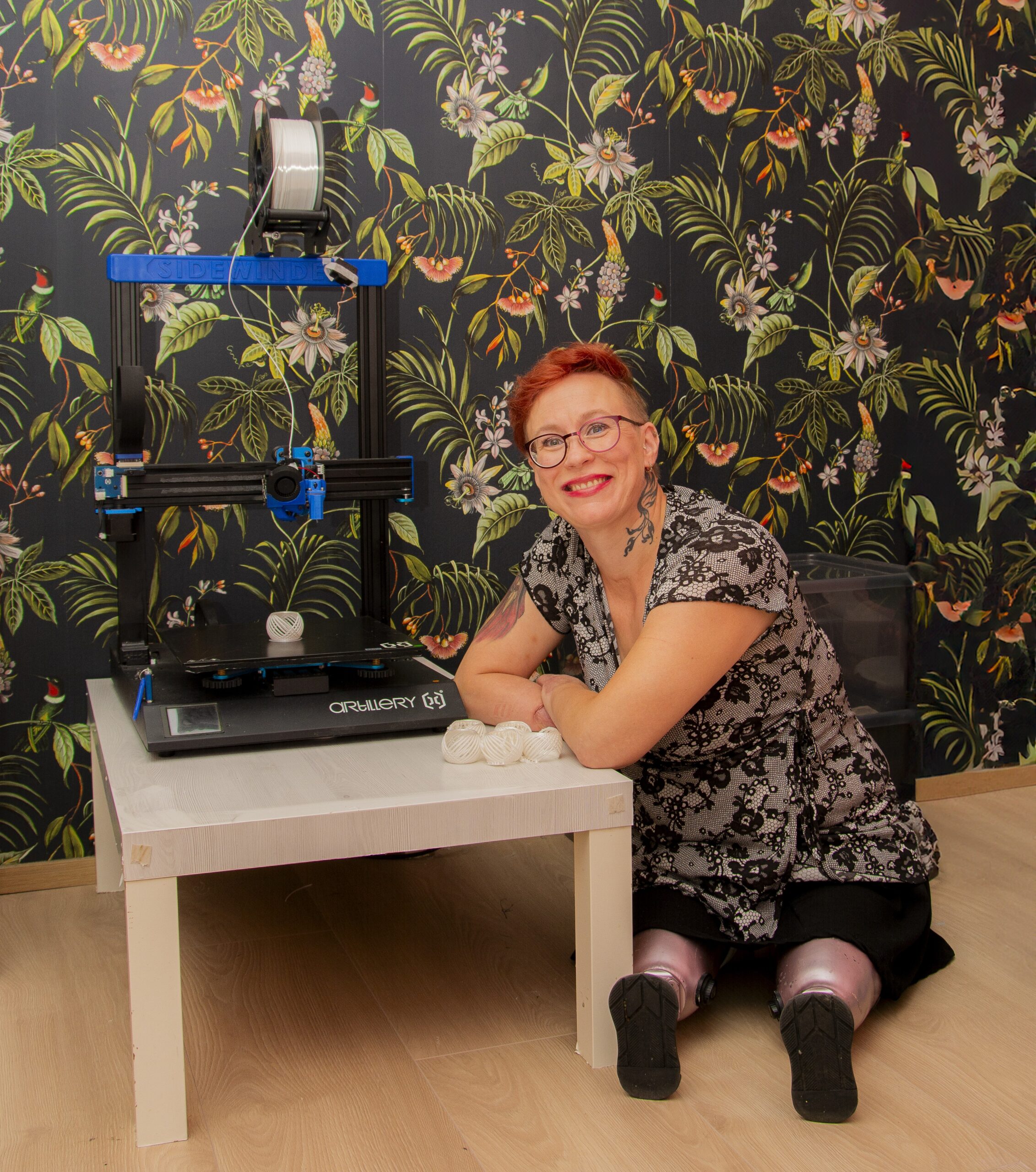 Proteeseja käyttävä nainen istuu 3D-tulostimen vieressä.