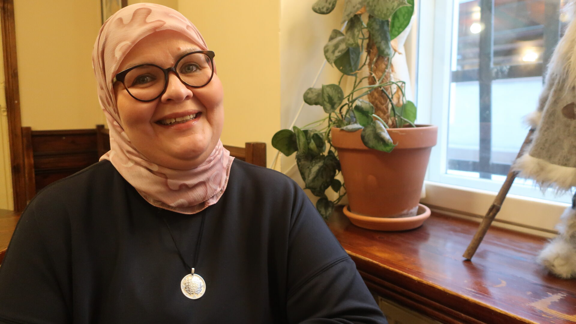 Nainen vaaleanpunaisessa huivissa ja mustassa tunikassa.