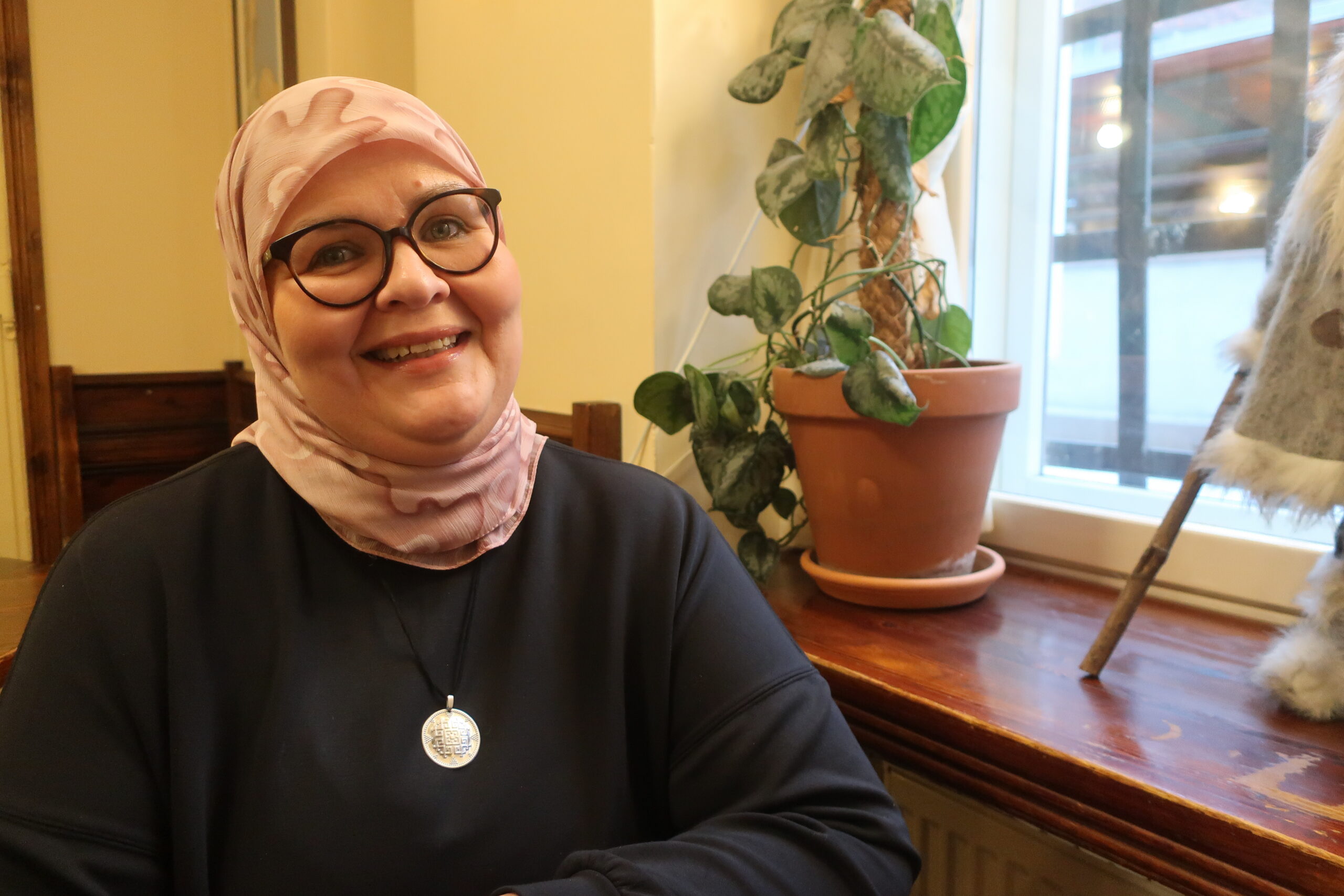 Nainen vaaleanpunaisessa huivissa ja mustassa tunikassa.