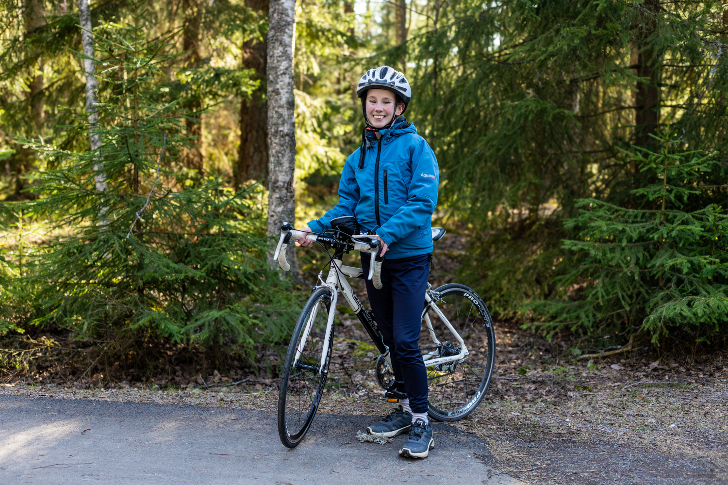 Nuori nainen sinisessä urheiluasussa pyörän selässä metsätiellä.